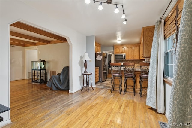 kitchen with a kitchen bar, appliances with stainless steel finishes, light hardwood / wood-style floors, and decorative backsplash