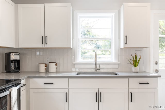 kitchen with a healthy amount of sunlight, white cabinets, backsplash, and sink