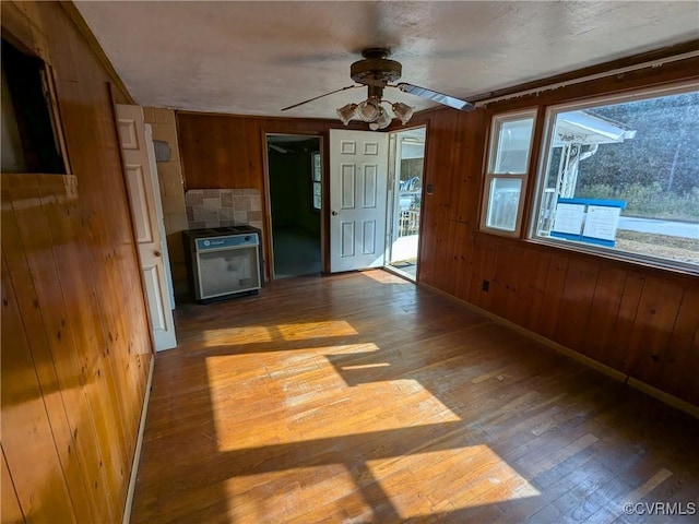 unfurnished living room featuring ceiling fan, wood-type flooring, and wood walls