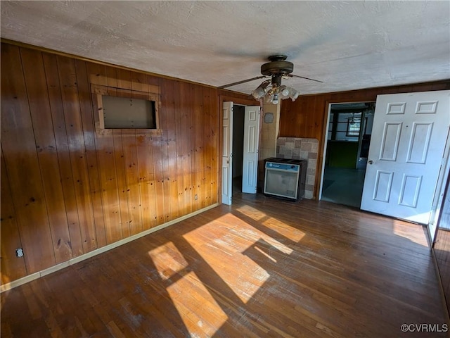 unfurnished living room featuring hardwood / wood-style flooring, a textured ceiling, ceiling fan, and wood walls