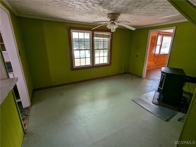 interior space with ceiling fan, crown molding, a textured ceiling, and a wood stove