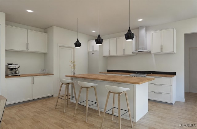 kitchen featuring wall chimney exhaust hood, light hardwood / wood-style flooring, white cabinetry, hanging light fixtures, and butcher block counters