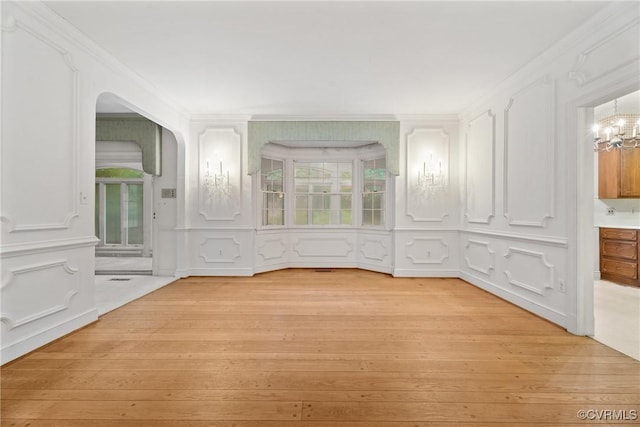 empty room with an inviting chandelier, light hardwood / wood-style flooring, and ornamental molding