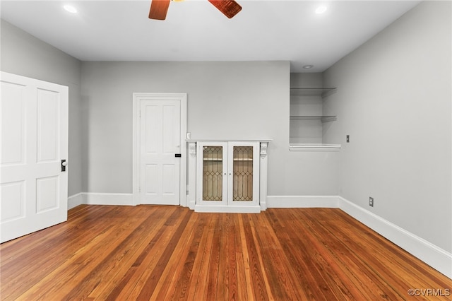 unfurnished living room with wood-type flooring, built in features, and ceiling fan