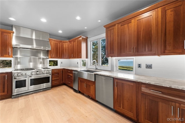 kitchen with light stone countertops, sink, wall chimney exhaust hood, light hardwood / wood-style flooring, and appliances with stainless steel finishes