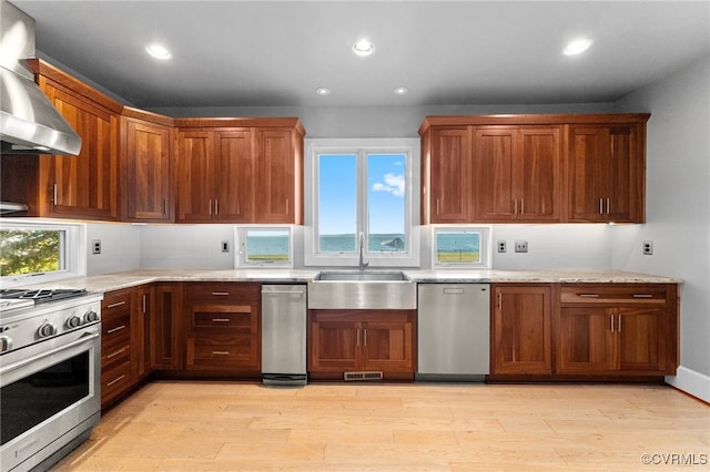 kitchen featuring light stone countertops, sink, stainless steel appliances, wall chimney range hood, and light wood-type flooring