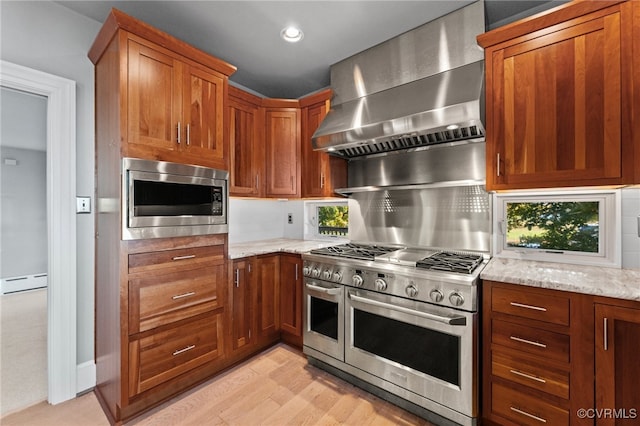 kitchen featuring appliances with stainless steel finishes, light stone counters, a baseboard heating unit, wall chimney range hood, and light hardwood / wood-style floors