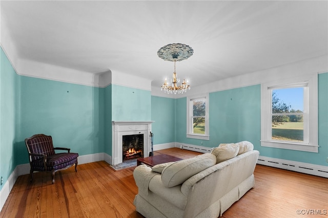 living room with a wealth of natural light, light hardwood / wood-style floors, a baseboard radiator, and an inviting chandelier