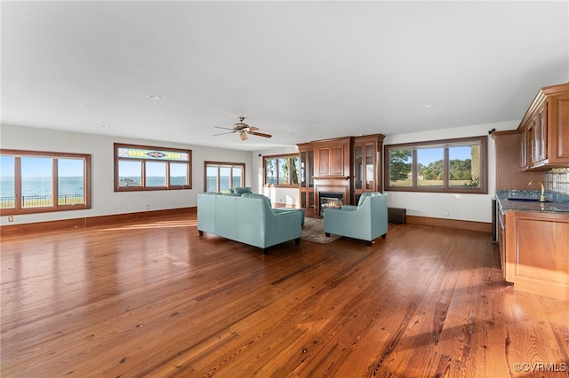 unfurnished living room with ceiling fan, dark wood-type flooring, a healthy amount of sunlight, and sink