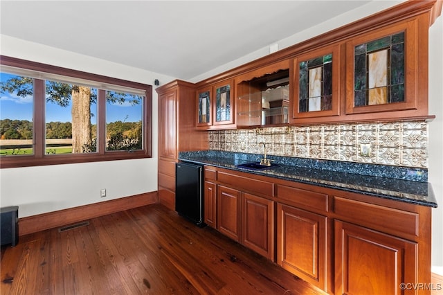 kitchen featuring sink, decorative backsplash, dark stone counters, dishwasher, and dark hardwood / wood-style floors