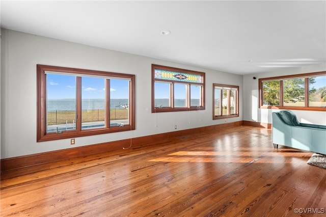 unfurnished living room with light hardwood / wood-style flooring, a water view, and a wealth of natural light