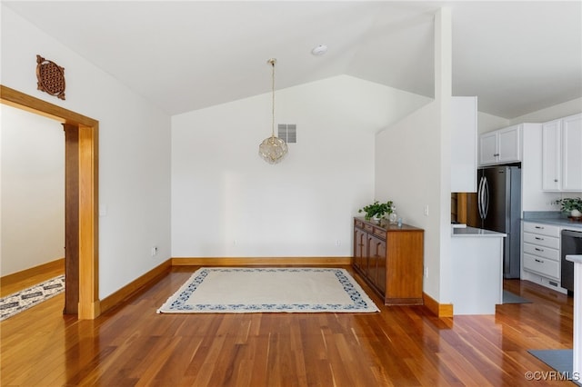 kitchen featuring dark wood-type flooring, hanging light fixtures, stainless steel fridge, lofted ceiling, and white cabinets