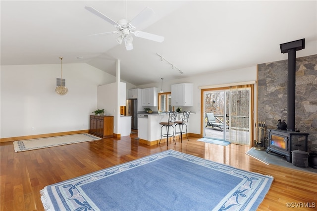 living room featuring a wood stove, light hardwood / wood-style flooring, ceiling fan, and lofted ceiling