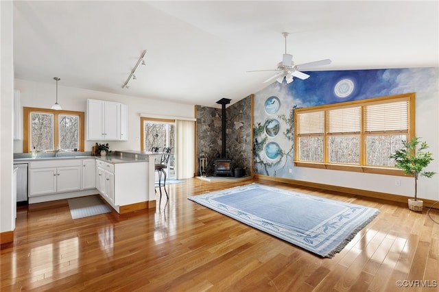 workout area featuring lofted ceiling, a wood stove, sink, ceiling fan, and light wood-type flooring