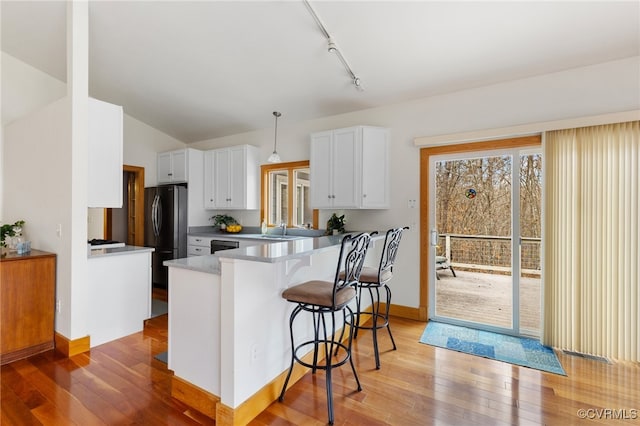 kitchen featuring kitchen peninsula, stainless steel fridge, decorative light fixtures, and white cabinetry