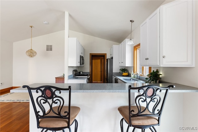 kitchen featuring stainless steel appliances, kitchen peninsula, wood-type flooring, vaulted ceiling, and white cabinets