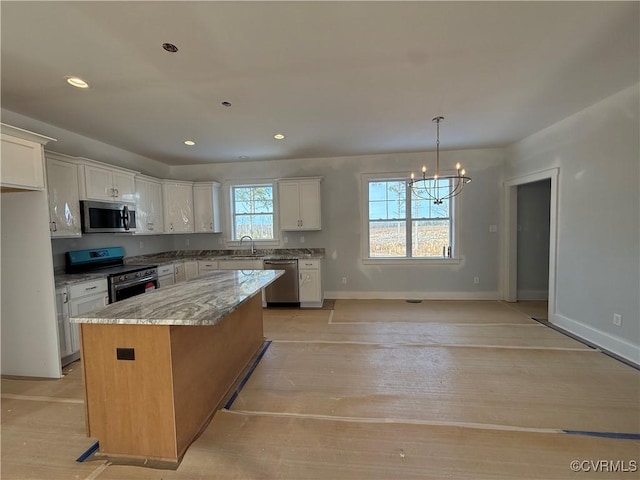 kitchen featuring light stone counters, stainless steel appliances, a sink, white cabinetry, and a center island