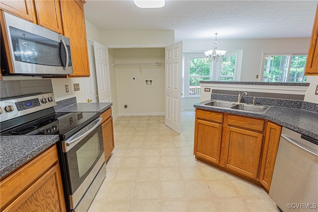 kitchen with a textured ceiling, stainless steel appliances, sink, pendant lighting, and a notable chandelier