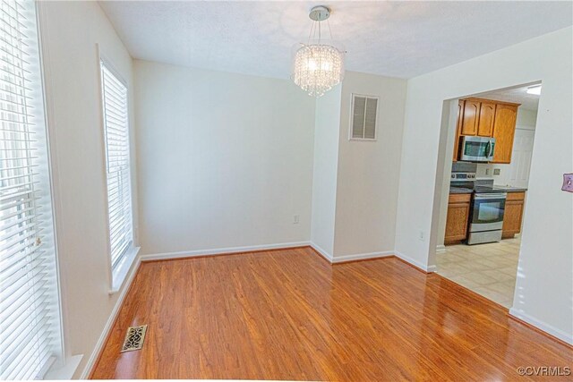 empty room featuring light hardwood / wood-style flooring, a wealth of natural light, and a notable chandelier