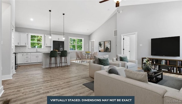 living area with visible vents, baseboards, ceiling fan, light wood-style flooring, and high vaulted ceiling