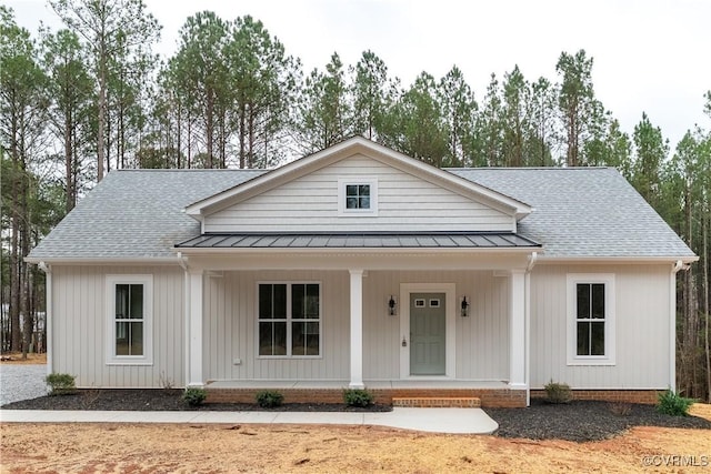 view of front facade featuring a porch, a shingled roof, a standing seam roof, and metal roof