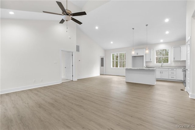 unfurnished living room featuring baseboards, light wood-style floors, high vaulted ceiling, a ceiling fan, and a sink