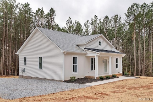 view of front of home featuring gravel driveway, a porch, and roof with shingles