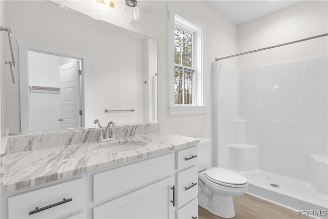 bathroom featuring wood finished floors, toilet, a stall shower, and vanity