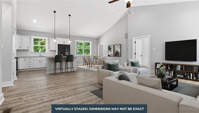 living room with ceiling fan, light wood-type flooring, and high vaulted ceiling