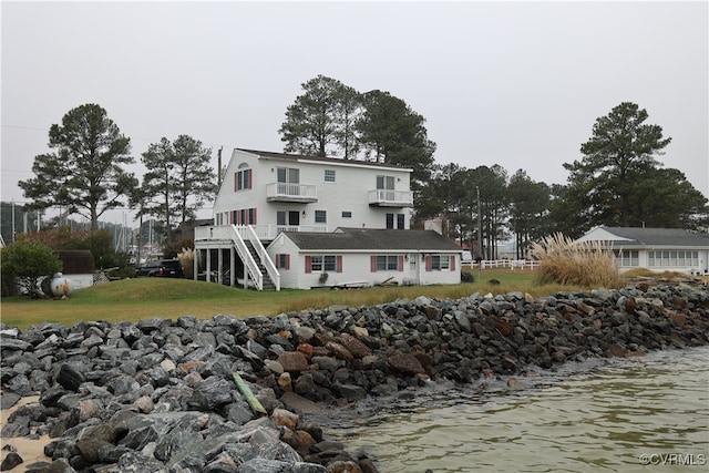 back of house featuring a water view, a balcony, and a lawn