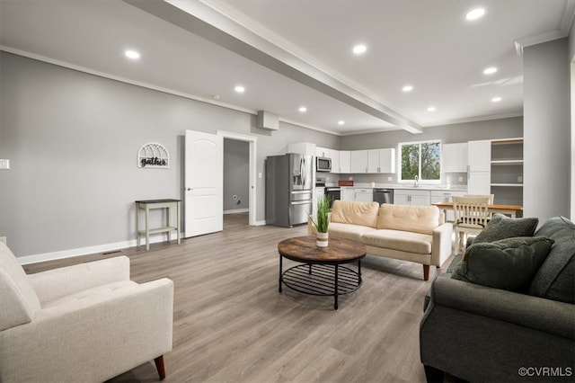 living room with sink, beamed ceiling, ornamental molding, and light wood-type flooring