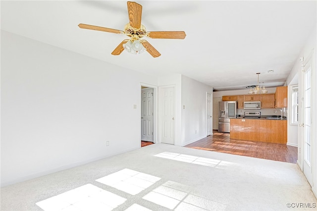 unfurnished living room featuring sink, ceiling fan with notable chandelier, and light wood-type flooring