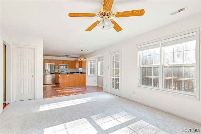 unfurnished living room with ceiling fan with notable chandelier and light hardwood / wood-style flooring