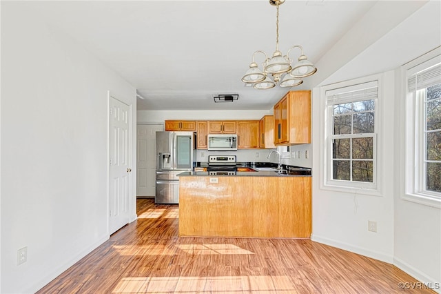 kitchen featuring hanging light fixtures, light wood-type flooring, appliances with stainless steel finishes, kitchen peninsula, and a chandelier