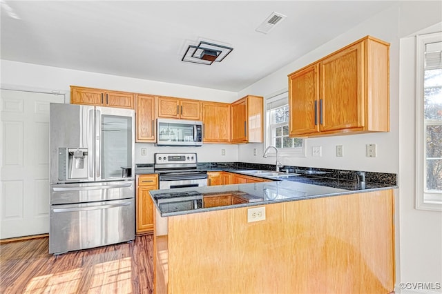 kitchen with hardwood / wood-style floors, dark stone counters, sink, kitchen peninsula, and stainless steel appliances