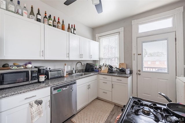 kitchen with dark stone counters, sink, appliances with stainless steel finishes, light hardwood / wood-style floors, and white cabinetry