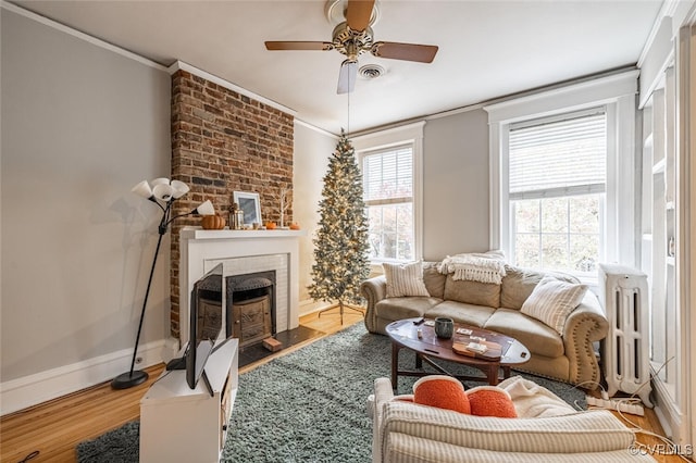 living room featuring hardwood / wood-style floors, ceiling fan, crown molding, and a brick fireplace