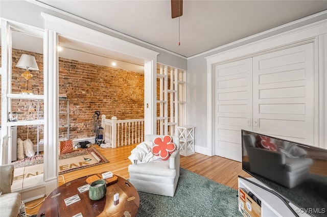 sitting room featuring hardwood / wood-style floors, ornamental molding, and brick wall