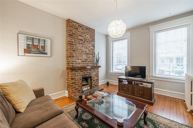 living room with a notable chandelier, a healthy amount of sunlight, light wood-type flooring, and radiator heating unit