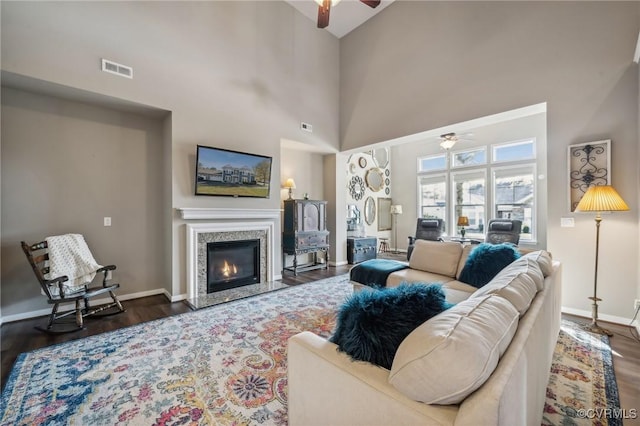 living room with a fireplace, a towering ceiling, ceiling fan, and dark wood-type flooring