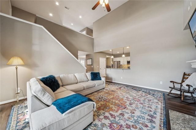 living room with a towering ceiling, ceiling fan, and dark wood-type flooring