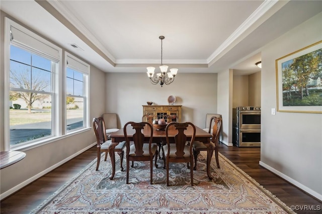 dining area with dark hardwood / wood-style floors, crown molding, a tray ceiling, and a notable chandelier