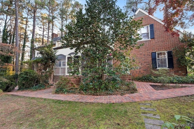 view of property exterior with brick siding, a chimney, and a yard