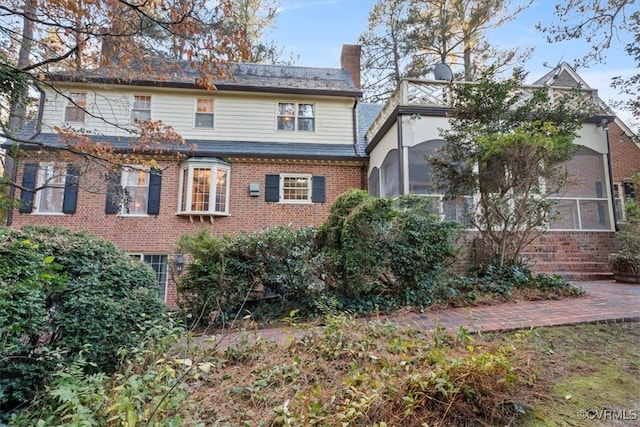 view of front of home featuring brick siding, a chimney, and a sunroom