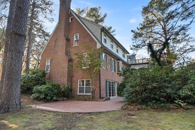 rear view of property with brick siding, a chimney, and a patio area