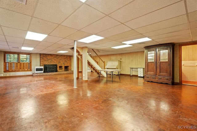 basement featuring a paneled ceiling, wooden walls, dark floors, and stairs