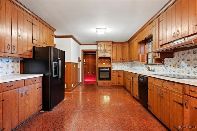 kitchen with a wainscoted wall, light countertops, brown cabinets, black appliances, and crown molding