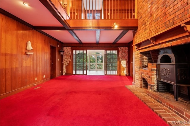 unfurnished living room featuring a brick fireplace, beam ceiling, carpet flooring, and wood walls