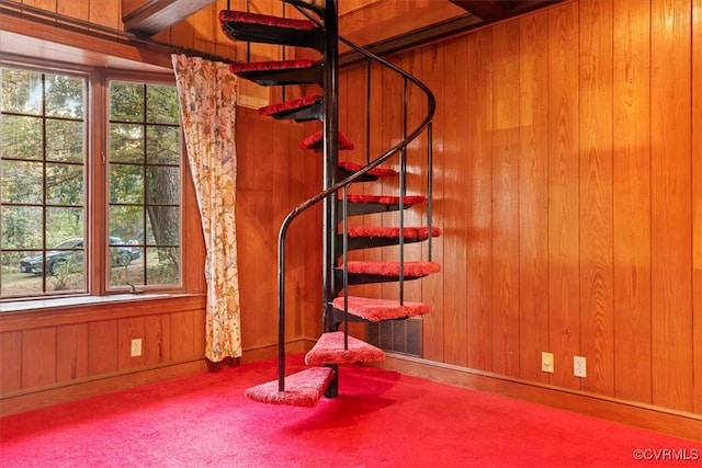 below grade area featuring plenty of natural light, carpet, wood walls, and stairs