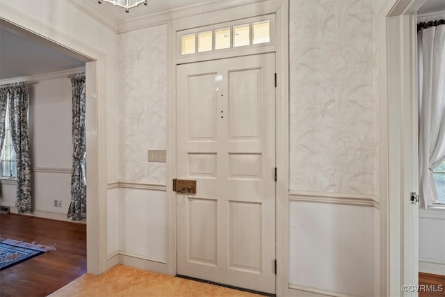 entrance foyer featuring ornamental molding, wainscoting, and wallpapered walls